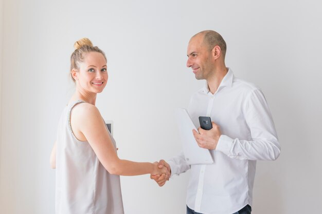 Sonriente joven empresaria agitando la mano con empresario sosteniendo papel y teléfono móvil