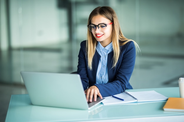 Sonriente joven empresaria escribiendo en el portátil en la oficina