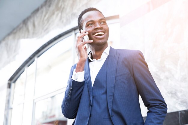 Sonriente joven empresario africano hablando por teléfono móvil