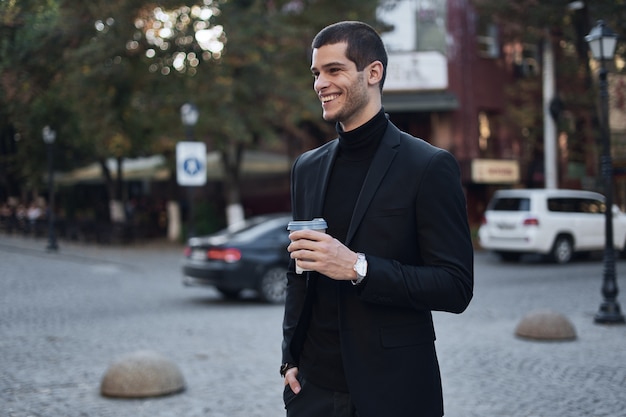 Sonriente joven empresario va al trabajo con café