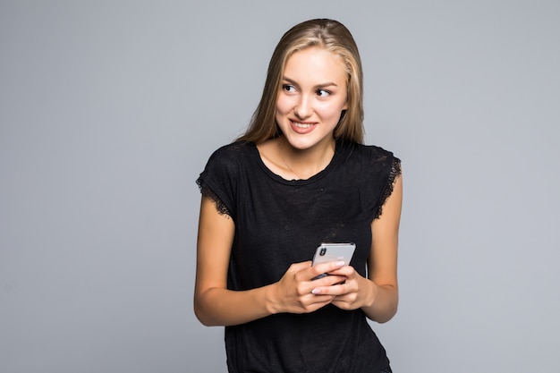 Sonriente joven encantadora de pie y con teléfono celular sobre fondo gris