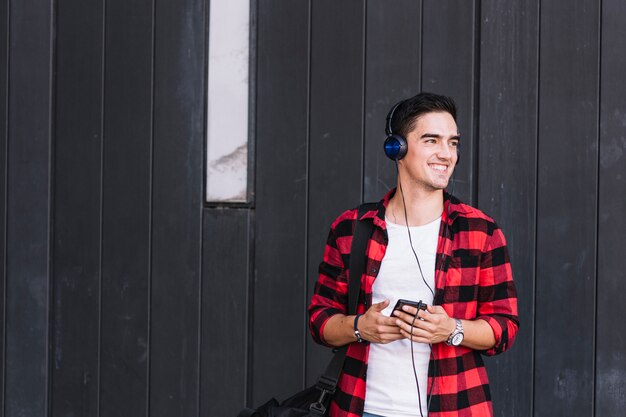 Sonriente joven escuchando música en frente de la pared de madera negra