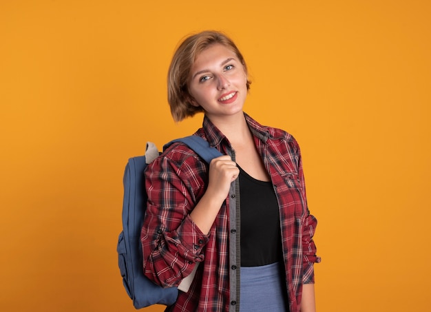 Sonriente joven estudiante eslavo vestida con mochila mira a la cámara