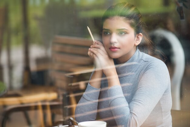 Sonriente joven estudiante con lápiz sentado en el café