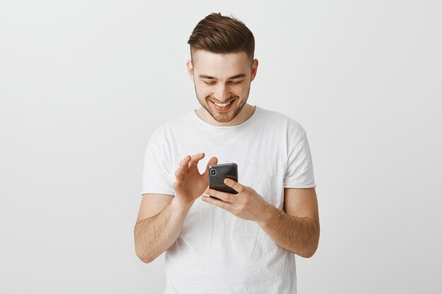 Sonriente joven feliz mediante teléfono móvil, mensajería con smartphone