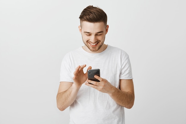 Sonriente joven feliz mediante teléfono móvil, mensajería con smartphone