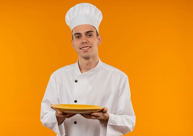 Sonriente joven fresco vistiendo uniforme de chef placa de sujeción con espacio de copia
