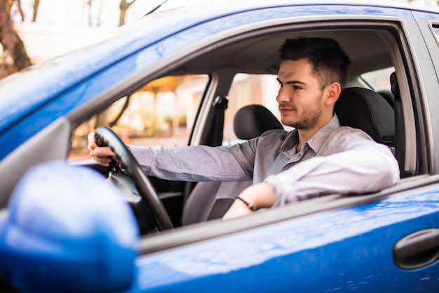 Sonriente joven con gafas sentado al volante de su coche conduciendo por la ciudad