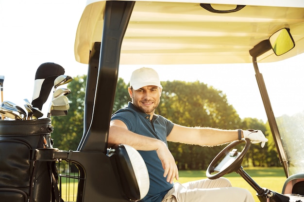 Sonriente joven golfista masculino sentado en un carrito de golf