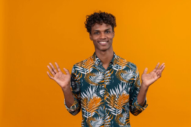 Sonriente joven guapo en camisa abriendo los brazos abiertos mirando hacia arriba sobre un fondo naranja