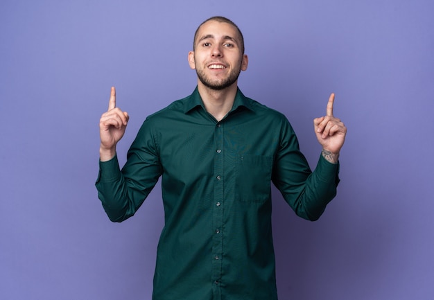 Sonriente joven guapo con camisa verde apunta hacia arriba