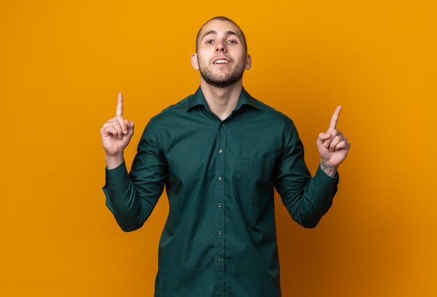 Sonriente joven guapo con camisa verde apunta hacia arriba