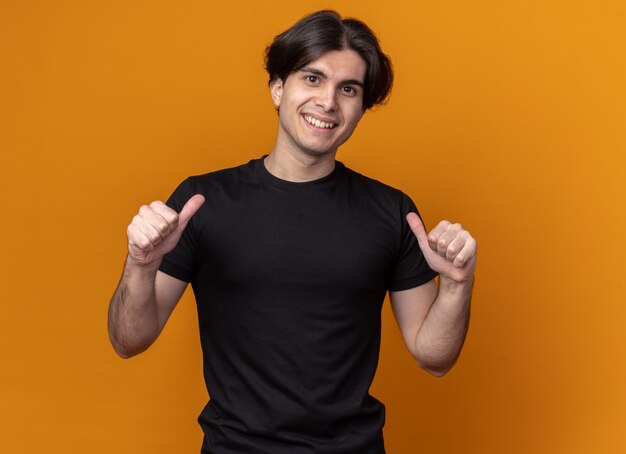 Sonriente joven guapo con camiseta negra apunta a sí mismo aislado en la pared naranja