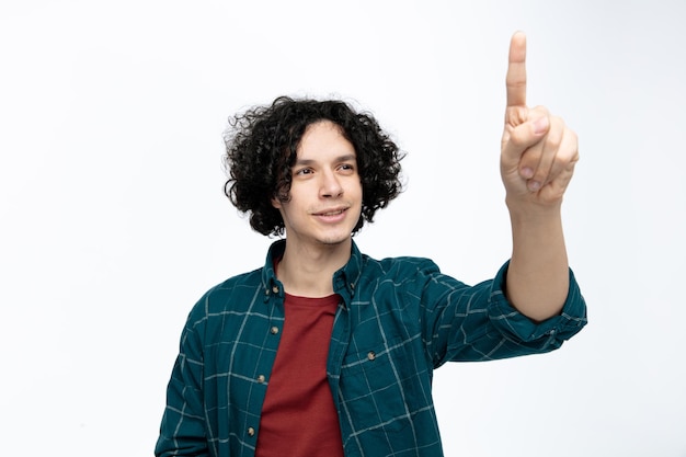 Sonriente joven guapo estirando el dedo índice hacia la cámara mirándolo aislado sobre fondo blanco.