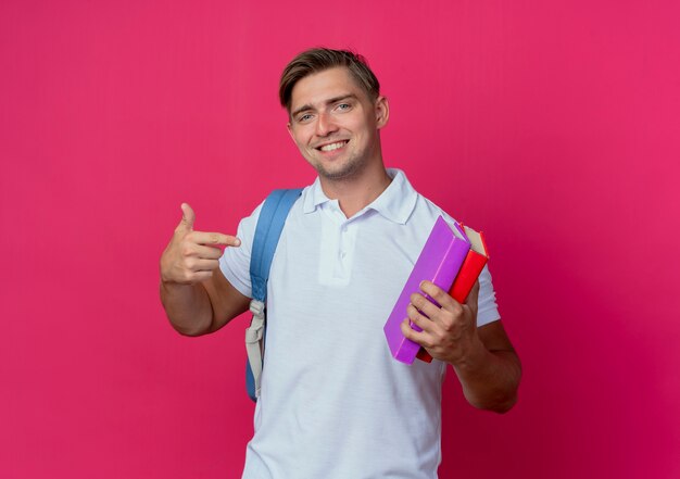 Sonriente joven guapo estudiante vistiendo bolsa trasera sosteniendo