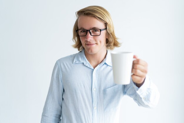 Sonriente joven guapo levantando la taza de té