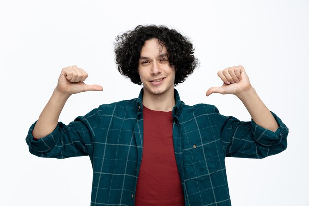 Sonriente joven guapo mirando a la cámara apuntándose a sí mismo aislado sobre fondo blanco.