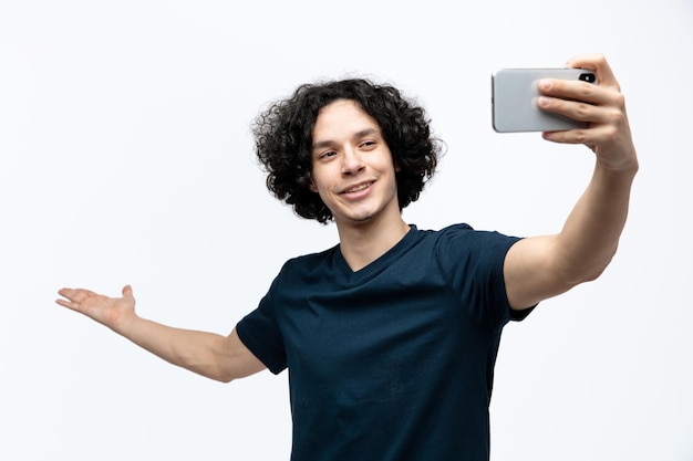 Foto gratuita sonriente joven guapo mostrando la mano vacía tomando selfie aislado sobre fondo blanco.