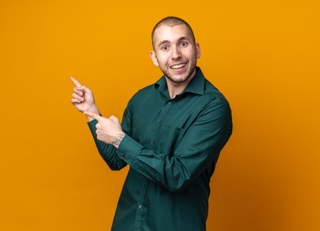 Sonriente joven guapo vistiendo puntos de camisa verde al lado