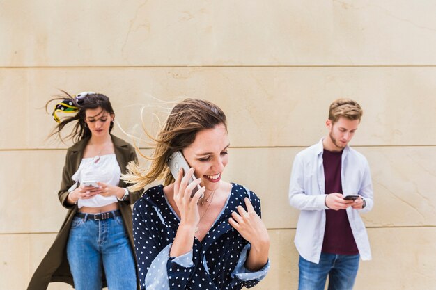 Sonriente joven hablando por teléfono móvil de pie delante de amigos