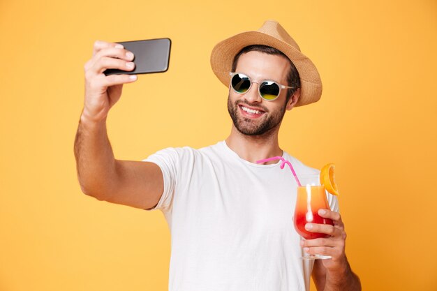 Sonriente joven hacer selfie por teléfono con cóctel.
