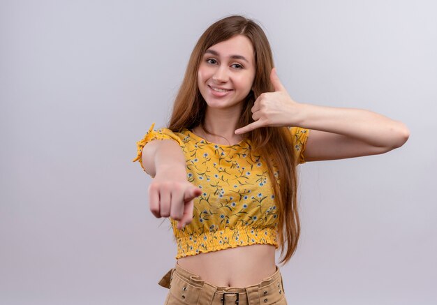 Sonriente joven haciendo señal de teléfono y apuntando a una pared blanca aislada con espacio de copia