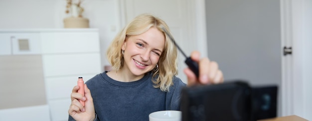 Sonriente joven hermosa blogger de estilo de vida graba un vlog de belleza en su habitación usando profesional