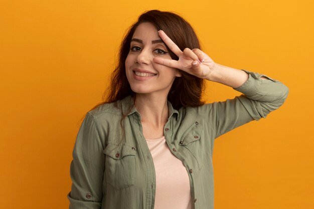 Sonriente joven hermosa chica con camiseta verde oliva que muestra gesto de paz aislado en la pared amarilla