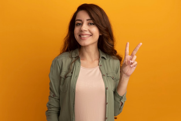 Sonriente joven hermosa chica con camiseta verde oliva que muestra gesto de paz aislado en la pared amarilla