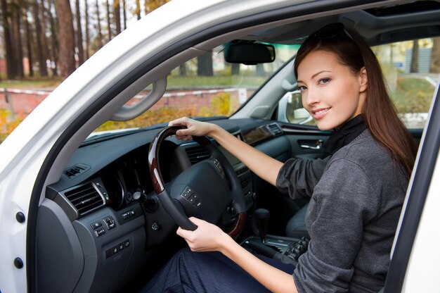 Sonriente joven hermosa mujer sentada en el coche nuevo - al aire libre