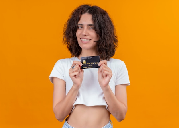 Sonriente joven hermosa mujer sosteniendo la tarjeta en la pared naranja aislada con espacio de copia