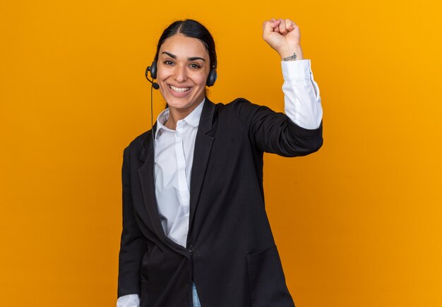 Sonriente joven hermosa mujer vestida con blazer negro con auriculares mostrando gesto de sí