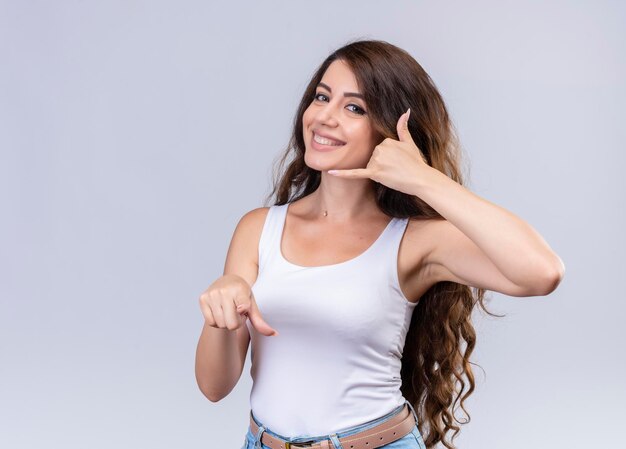 Sonriente joven hermosa niña apuntando y haciendo distintivo de llamada con espacio de copia