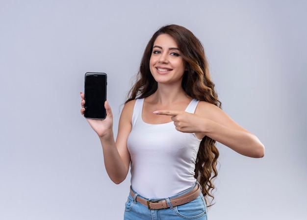 Sonriente joven hermosa niña sosteniendo teléfono móvil y apuntando a él con espacio de copia