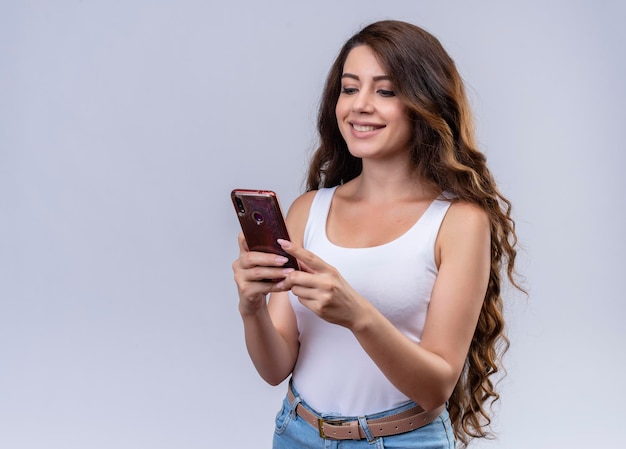 Sonriente joven hermosa niña sosteniendo teléfono móvil mirándolo con espacio de copia