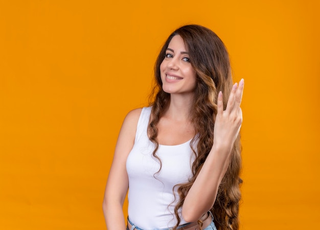 Sonriente joven hermosa que muestra tres en el espacio naranja aislado con espacio de copia