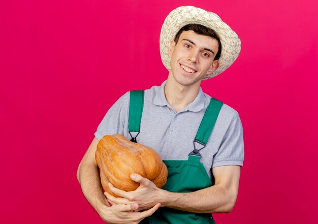 Sonriente joven jardinero vistiendo sombrero de jardinería tiene calabaza