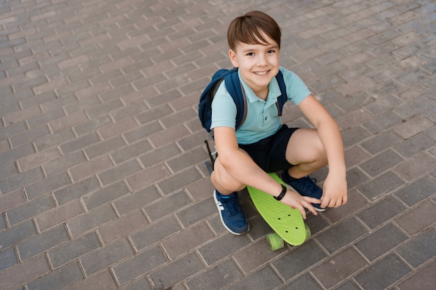 Sonriente joven jugando en patineta en la ciudad, niño caucásico montando penny board