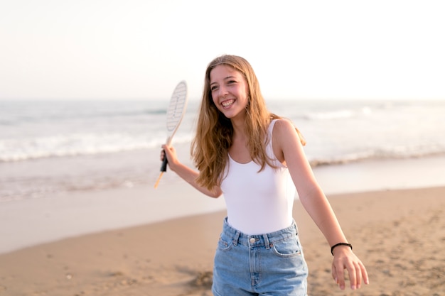 Sonriente joven jugando con raqueta de tenis en la orilla del mar