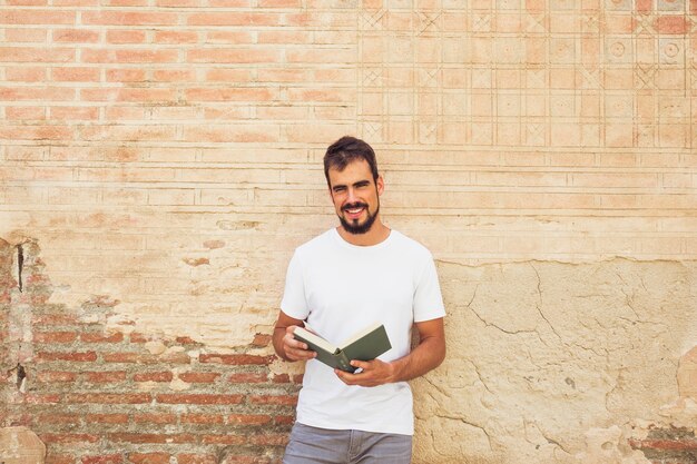 Sonriente joven con libro en frente de la pared