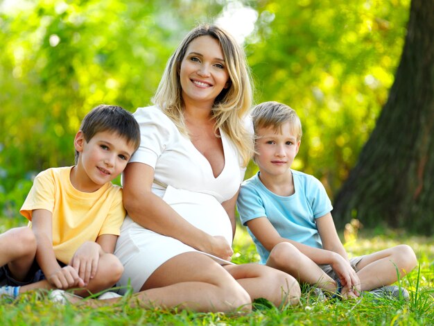 Sonriente joven madre embarazada con dos hijos posando al aire libre