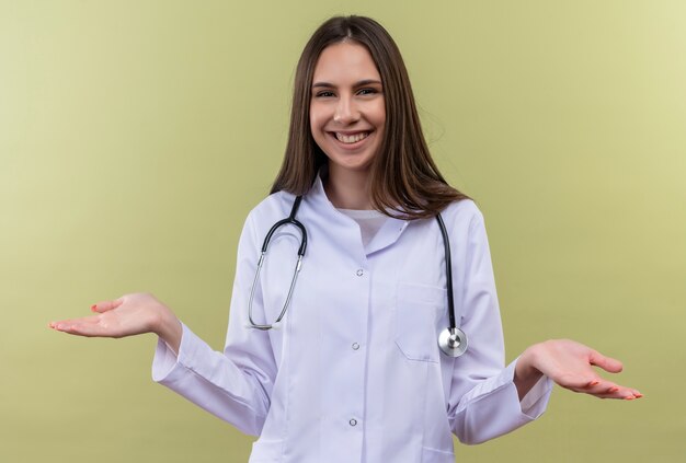 Sonriente joven médico con estetoscopio bata médica extiende las manos sobre fondo verde