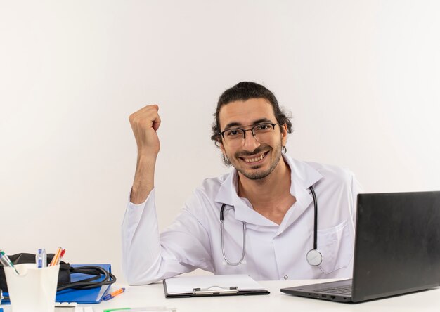 Sonriente joven médico con gafas médicas vistiendo bata médica con estetoscopio