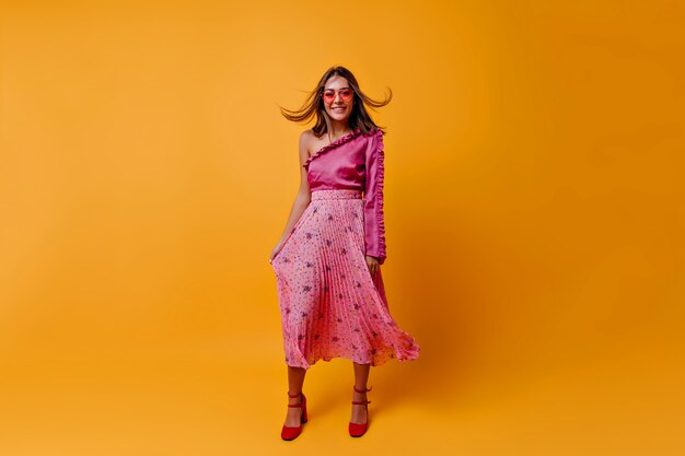 Sonriente, joven modelo con top moderno y elegante y falda midi está de muy buen humor. Morena de pelo corto ondeando en el viento