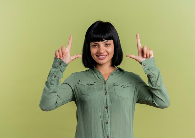 Sonriente joven morena caucásica apunta hacia arriba con las dos manos y mira