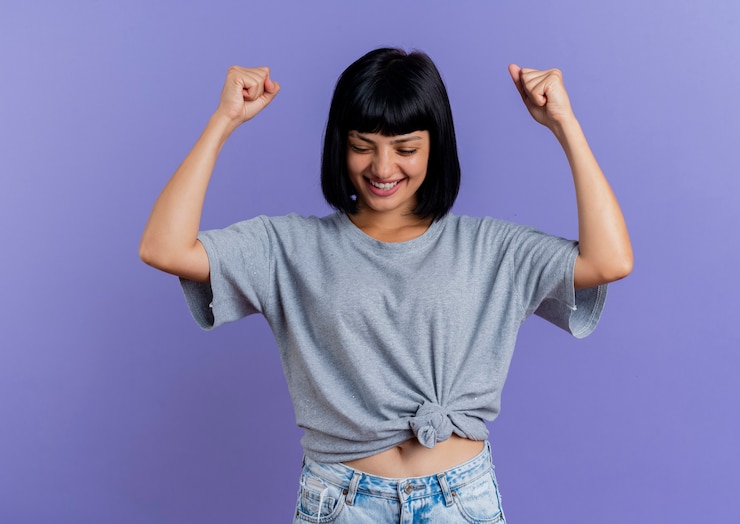 Foto gratuito sonriente joven morena caucásica mantiene los puños mirando hacia abajo aislado sobre fondo púrpura con espacio de copia