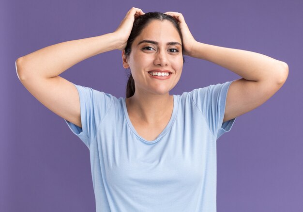 Sonriente joven morena caucásica pone las manos en la cabeza.