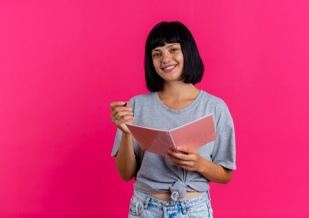 Sonriente joven morena caucásica sostiene bolígrafo y cuaderno