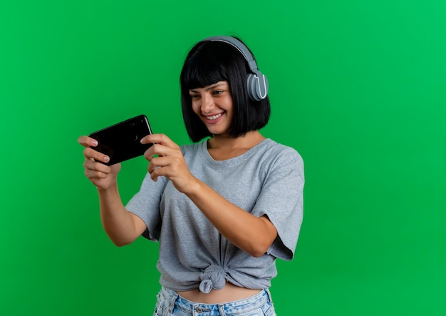 Sonriente joven morena mujer caucásica en auriculares sostiene y mira teléfono