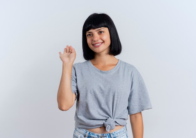 Sonriente joven morena mujer caucásica se encuentra con la mano levantada mirando al lado